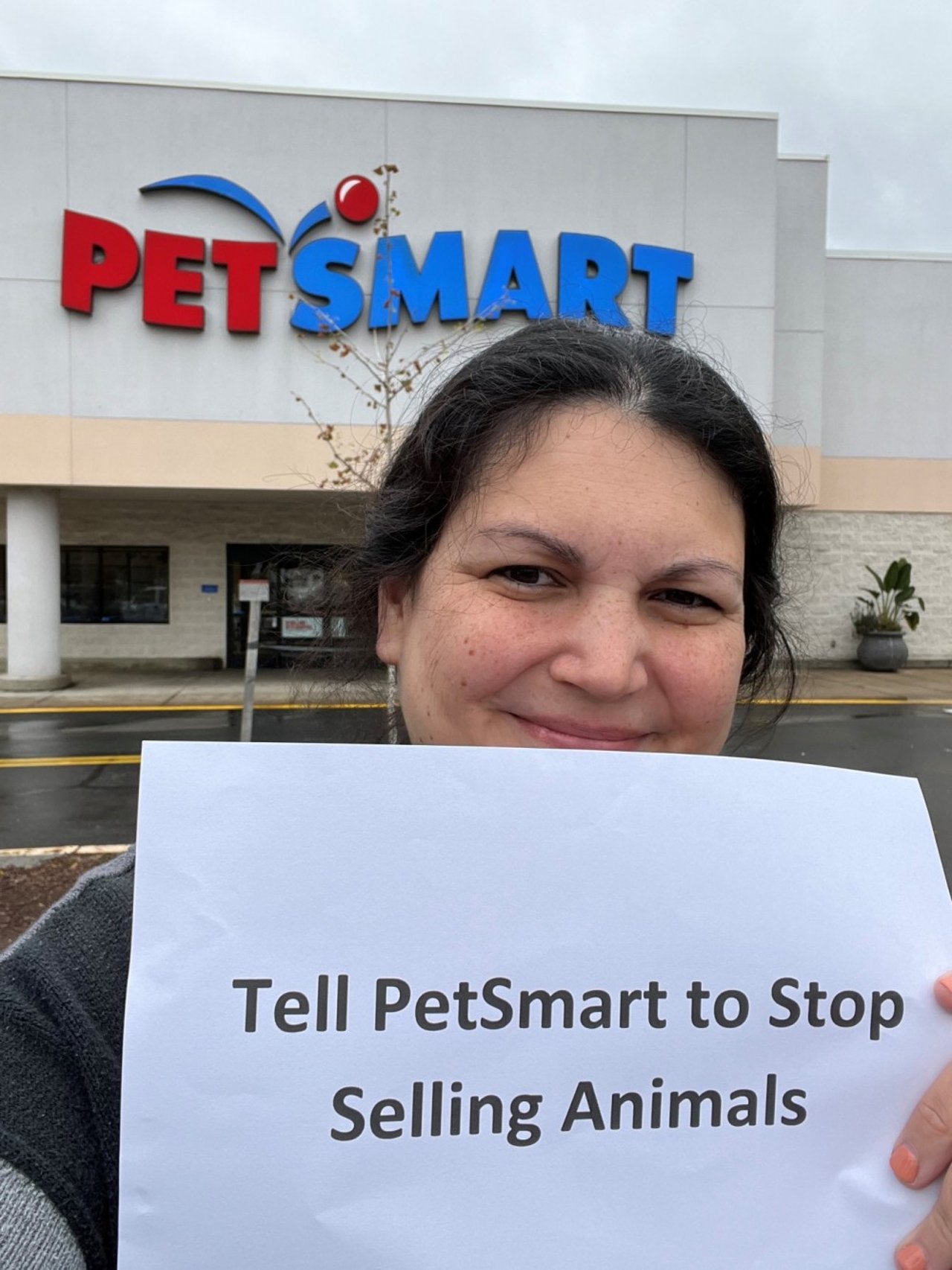 A selfie of liz cabrera holtz in front of a PetSmart store with her sign